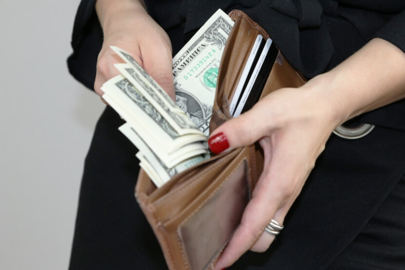 woman pulling money out of brown leather wallet