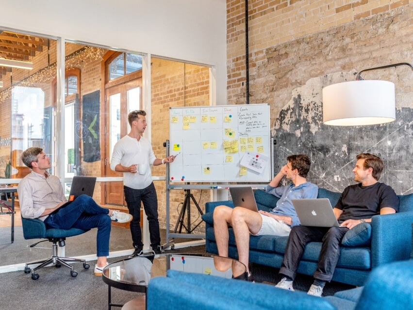 product manager stands up by a white board in meeting with three other people